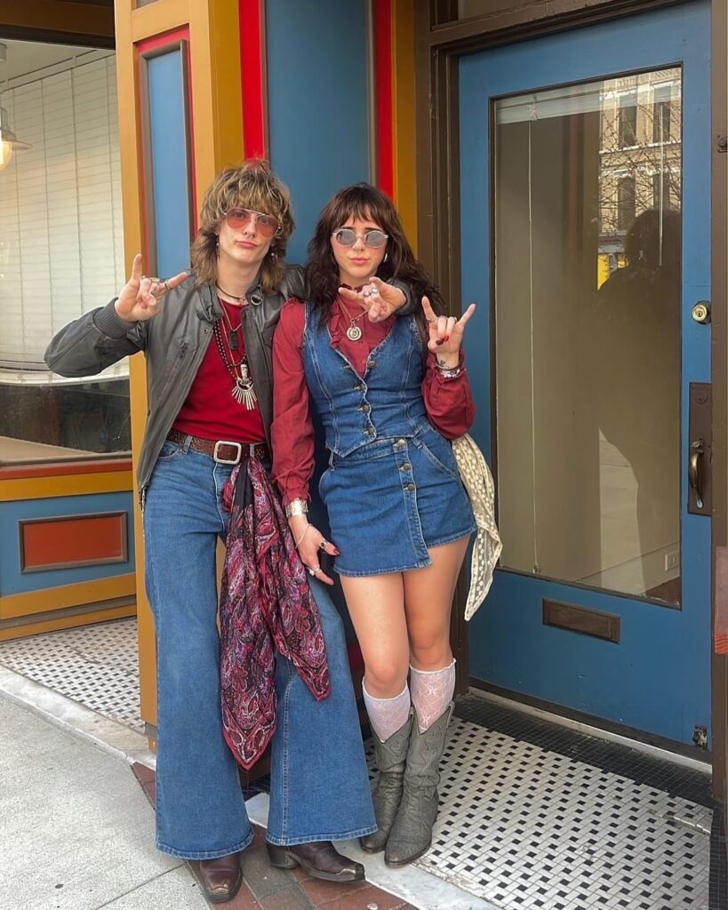 Two people posing in retro 1970s inspired outfits including bell-bottom jeans and a denim dress.