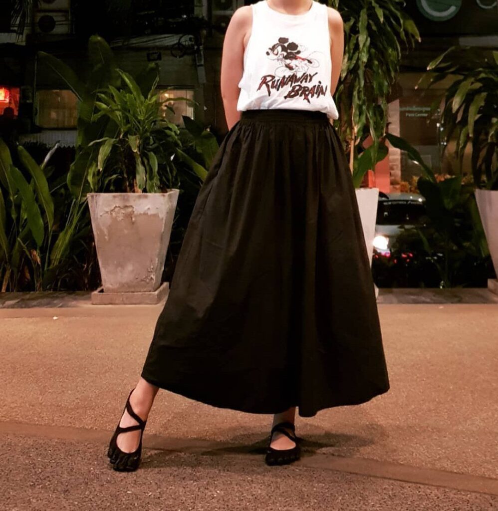 Person wearing a white graphic tank top and a long black midi skirt.
