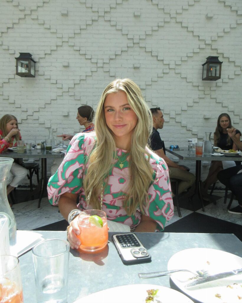 Woman in a pink and green floral blouse sitting at an outdoor brunch table.