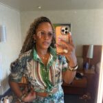Woman in a green and blue patterned matching set taking a mirror selfie.