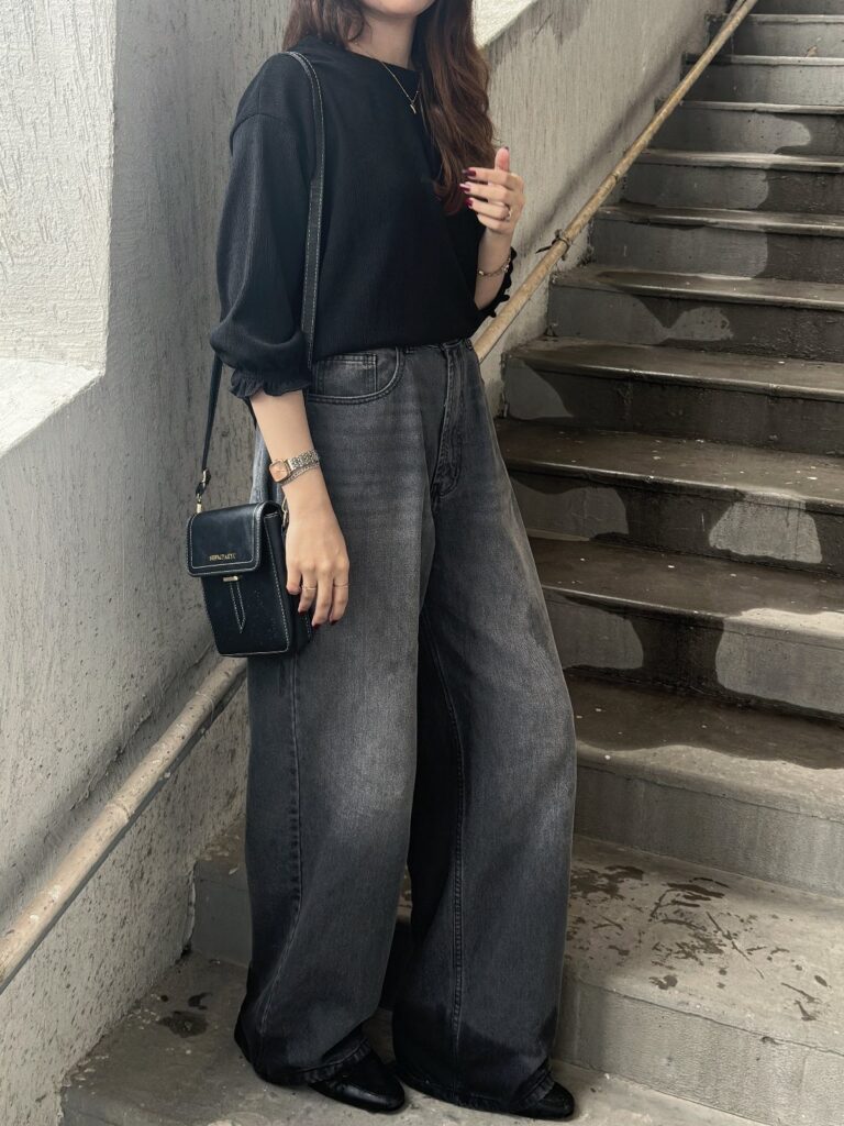 Person wearing oversized black sweater and baggy grey jeans on concrete stairs