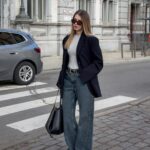 Woman wearing a navy blazer and wide-leg blue jeans on a city street.
