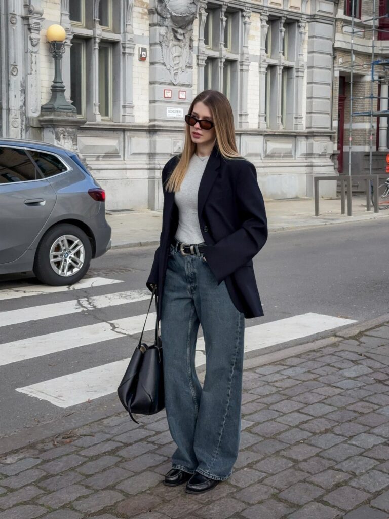 Woman wearing a navy blazer and wide-leg blue jeans on a city street.