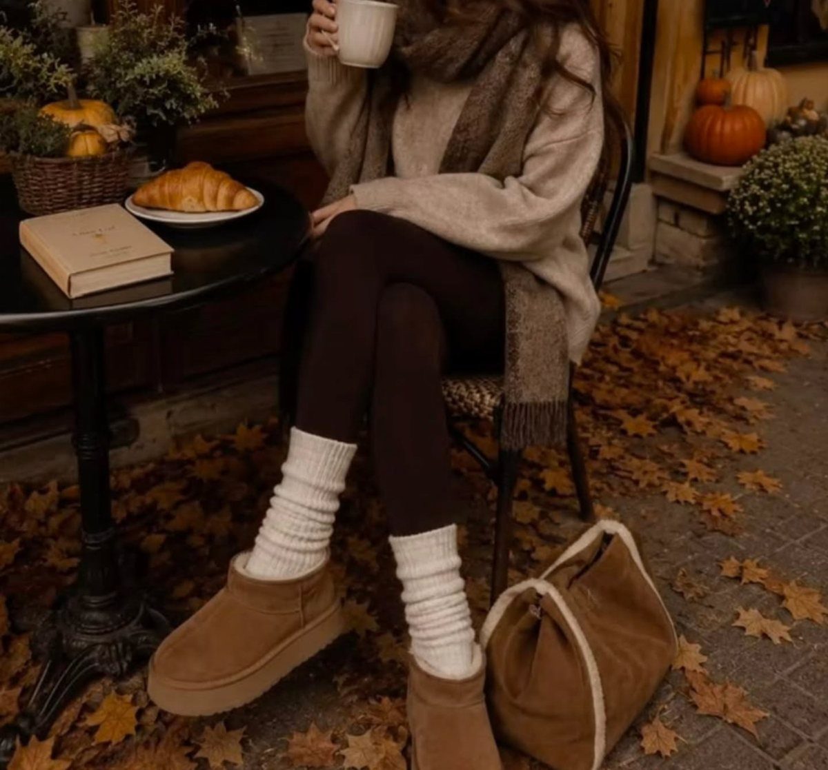 Person in cozy fall outfit with beige sweater and tan boots among autumn leaves
