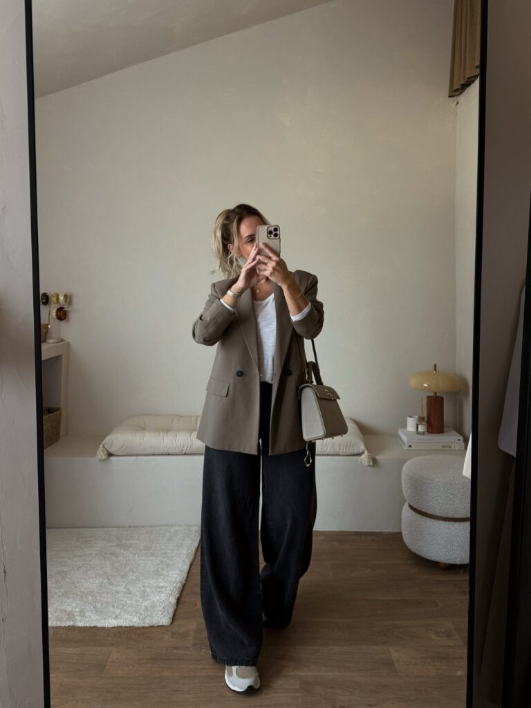 Woman in white t-shirt, wide-leg jeans, and taupe blazer posing for a mirror selfie.