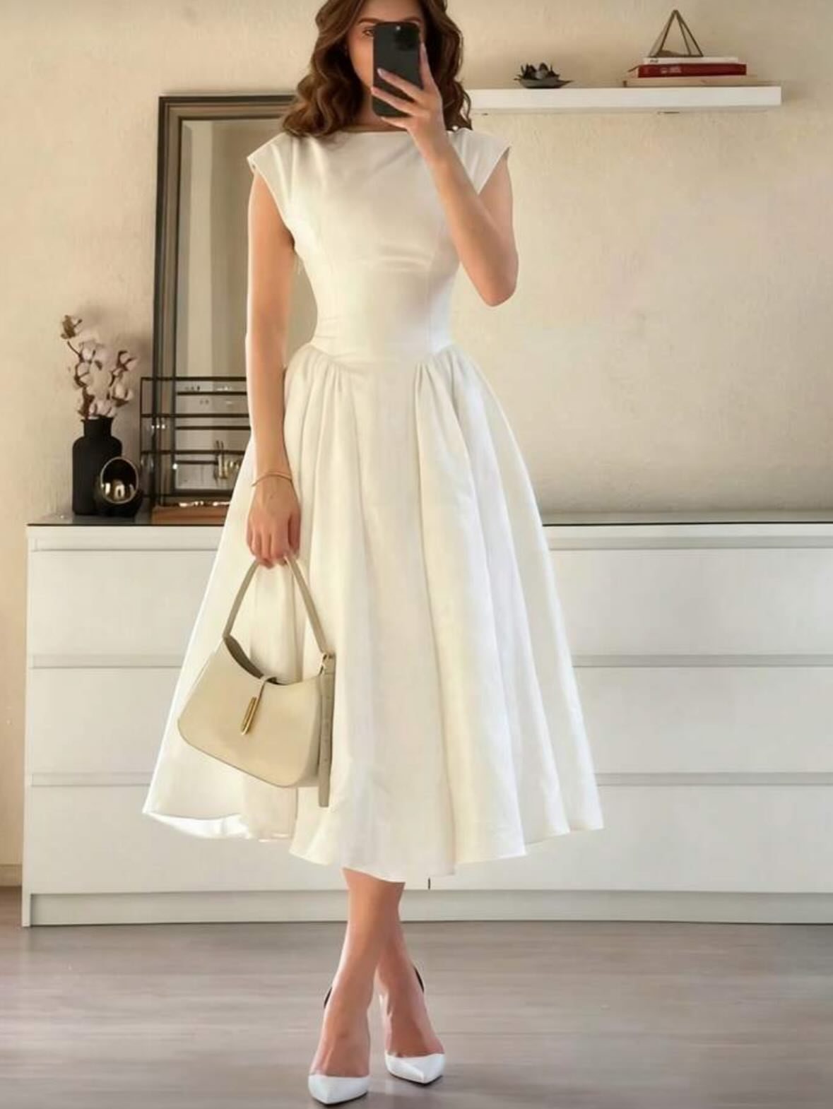 Woman posing in a sleeveless white midi dress with a flared skirt and white heels.