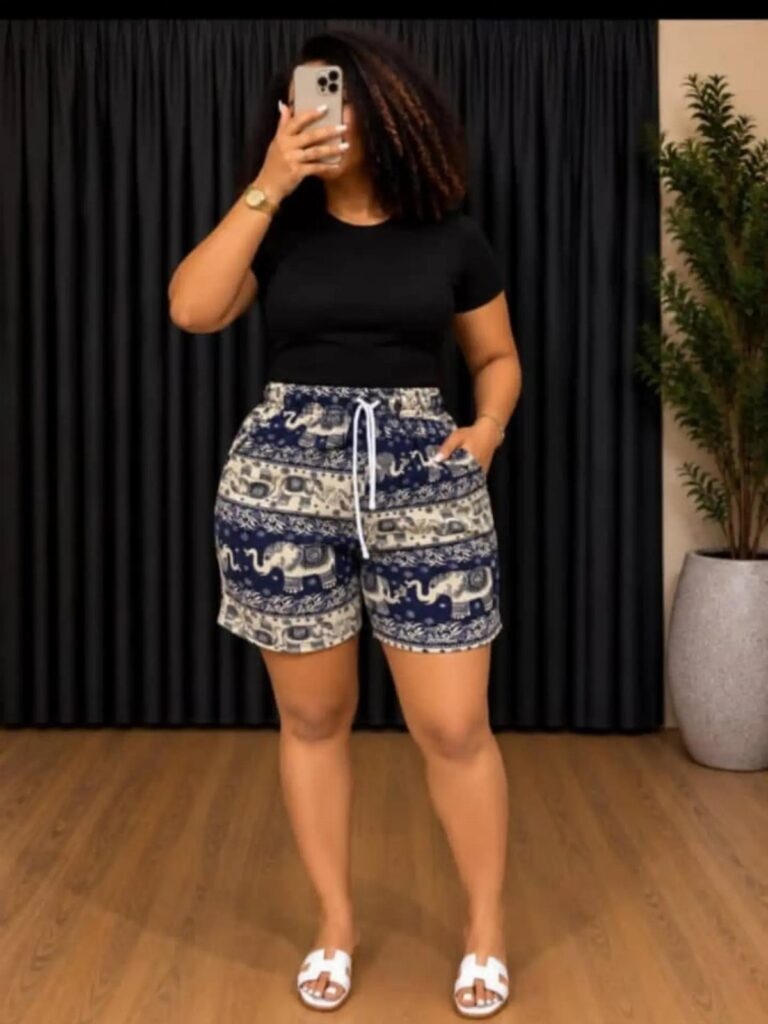 Woman wearing a black t-shirt and blue patterned elephant print shorts with white sandals.
