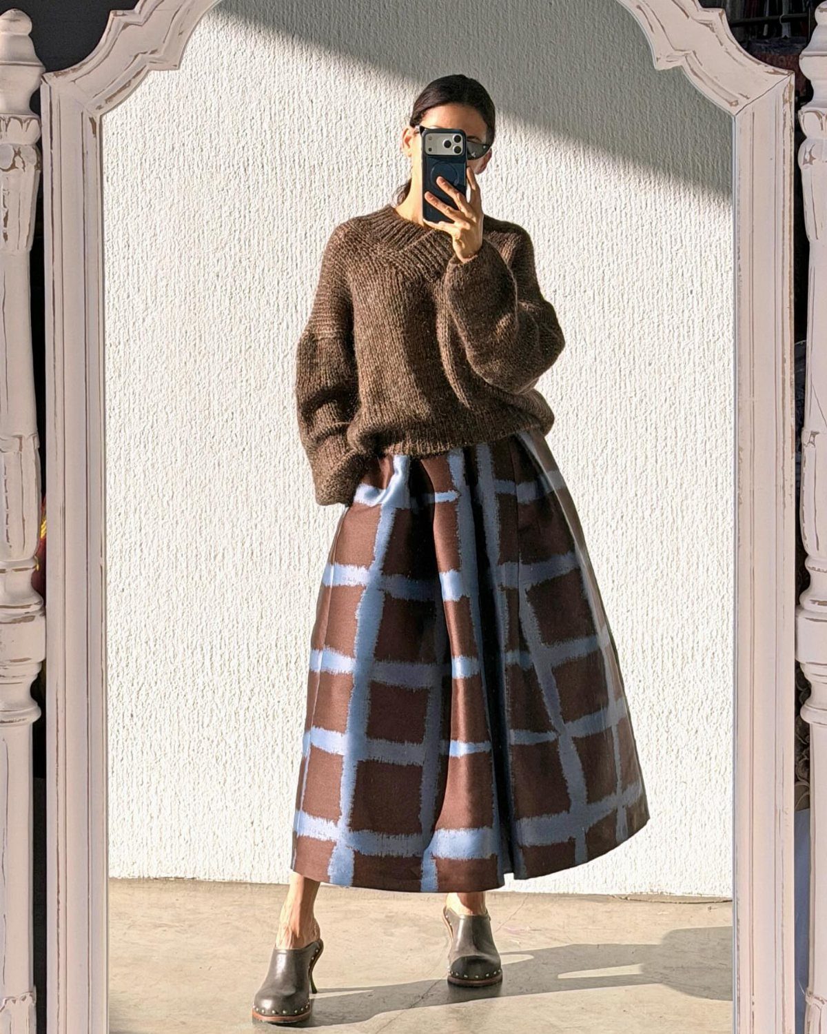 Person in a brown knit sweater and blue and brown plaid maxi skirt.