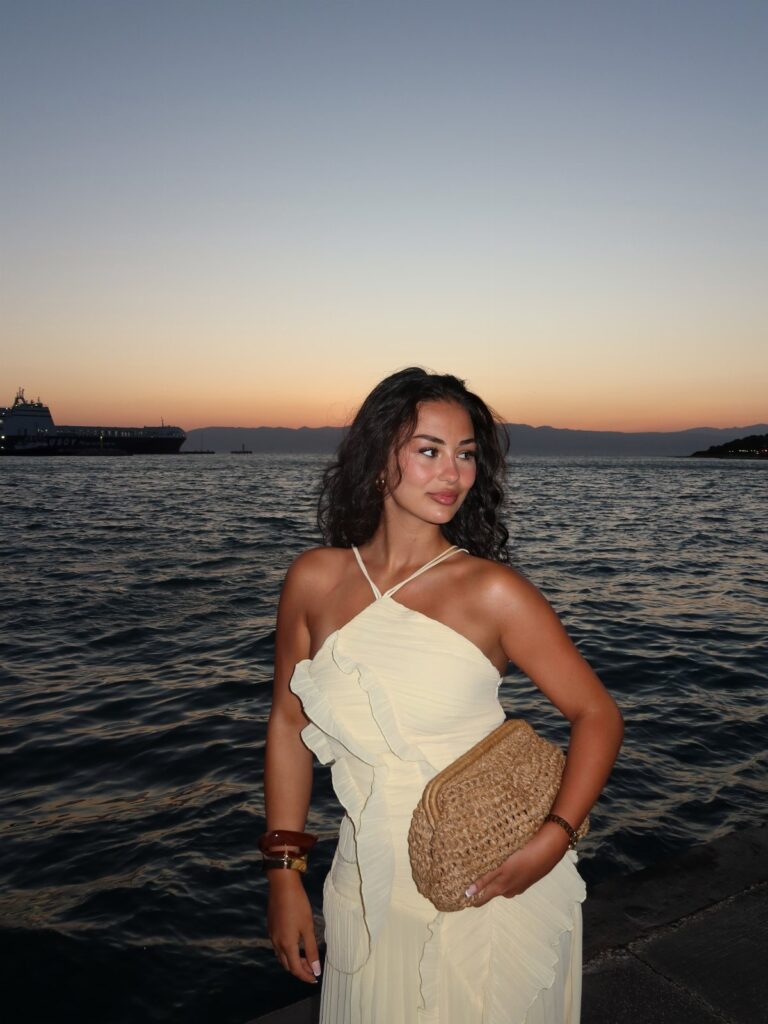 Woman in a cream ruffled halter dress posing by the ocean during sunset.