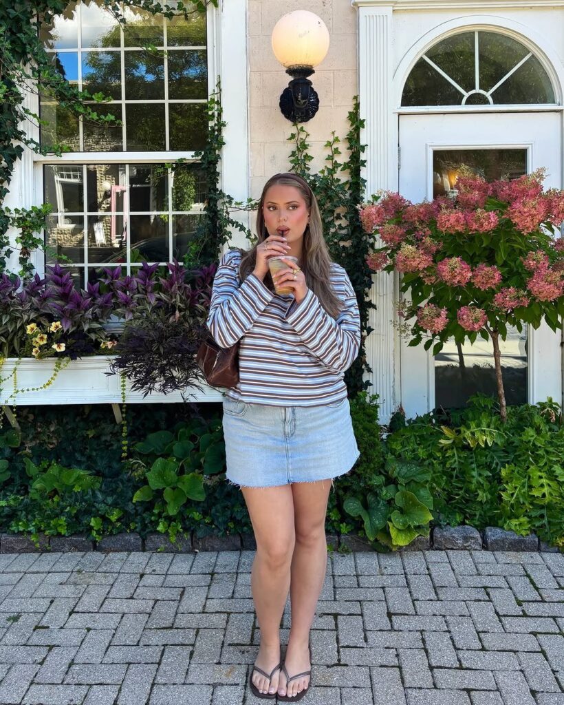 Woman wearing a striped sweater and light blue denim mini skirt outdoors.