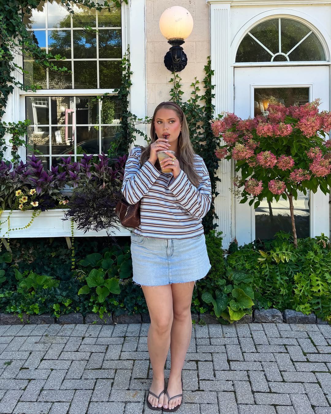 Woman wearing a striped sweater and light blue denim mini skirt outdoors.