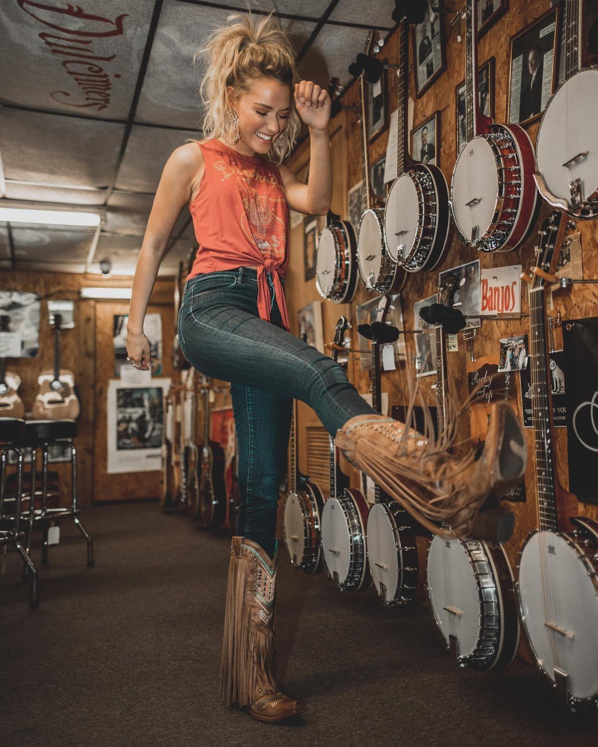 Woman in orange top and blue jeans wearing brown fringed cowboy boots.