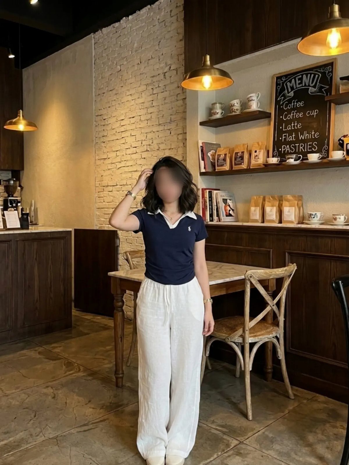 Woman wearing a navy polo shirt and wide-leg white trousers in a cafe.
