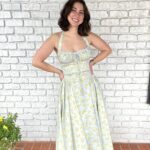 Woman wearing a light blue and yellow floral midi dress against a white brick wall