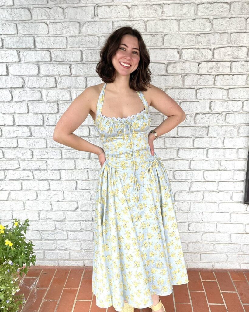 Woman wearing a light blue and yellow floral midi dress against a white brick wall
