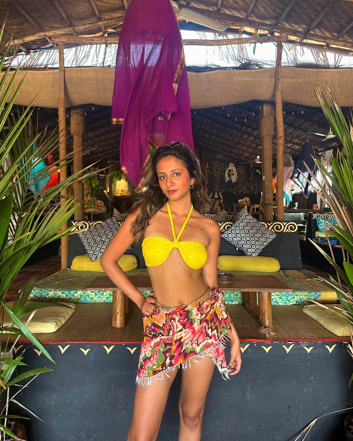 Woman wearing a yellow bikini top and a floral sarong standing in a tropical lounge.