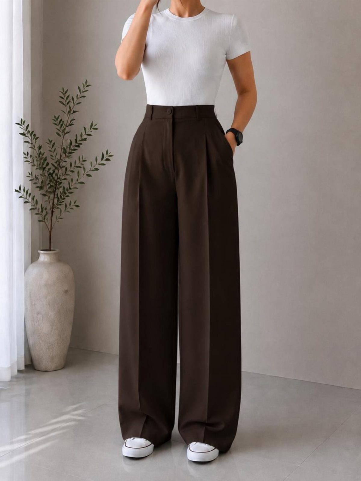 Person wearing white t-shirt, brown wide-leg trousers, and white sneakers in a bright room.