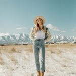 Woman in a snowy field wearing a tan hat, denim-accented jacket, and blue jeans.