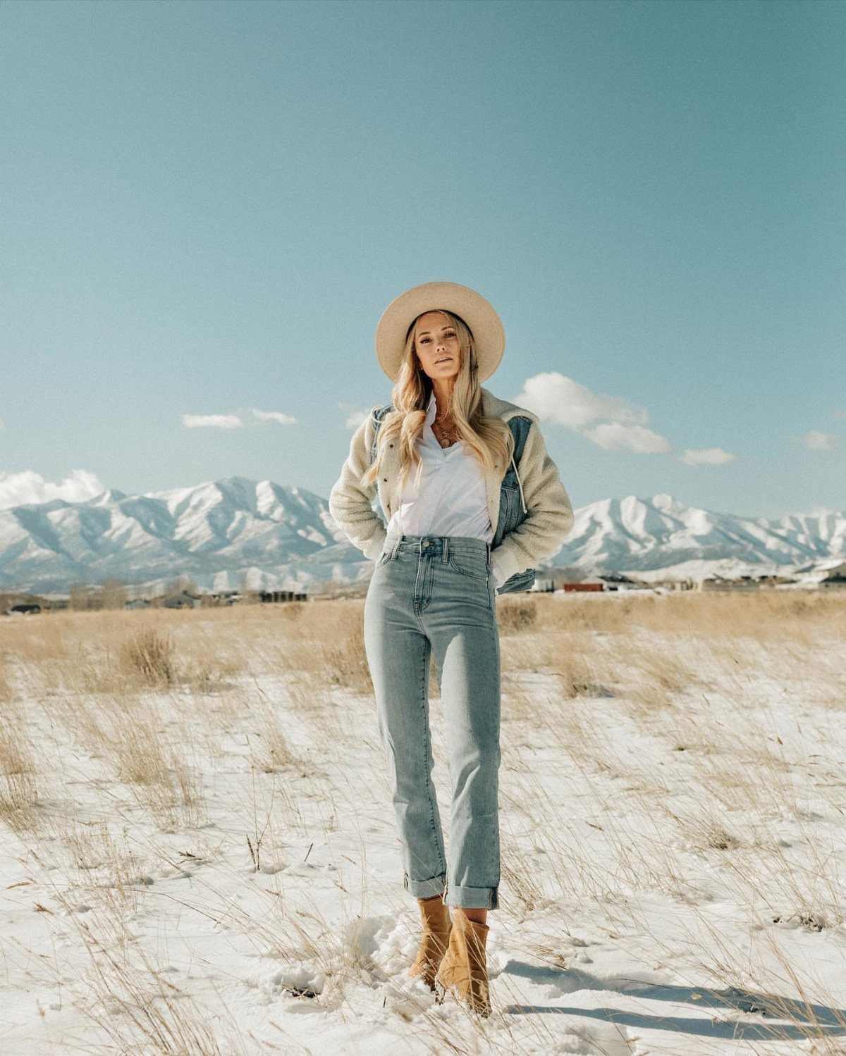 Woman in a snowy field wearing a tan hat, denim-accented jacket, and blue jeans.
