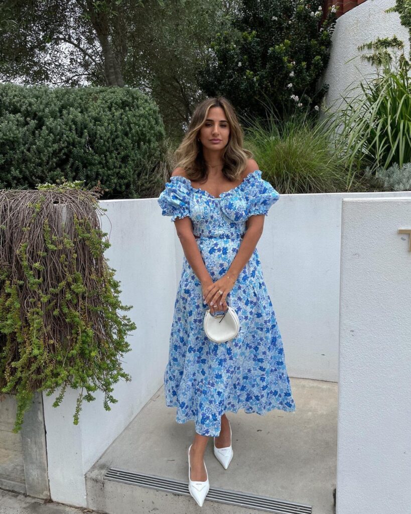 Woman in a blue floral puff-sleeve midi dress with a sweetheart neckline and white heels.